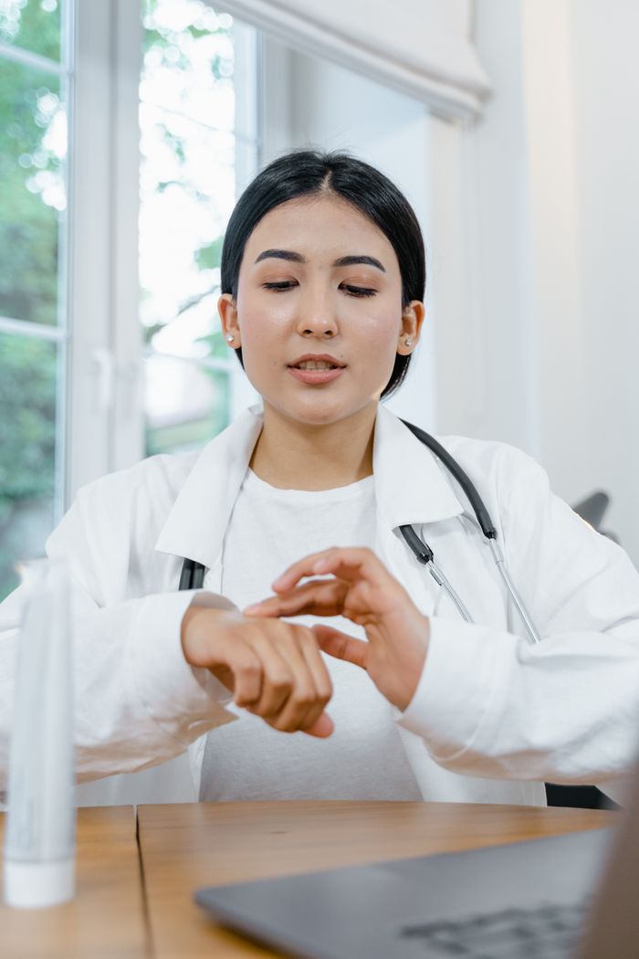 A female doctor applies hand cream while sitting at a desk in a medical office setting.
